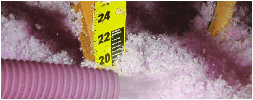 A pink hose blowing in fiberglass insulation with a measuring stick showing its depth at 20 inches.